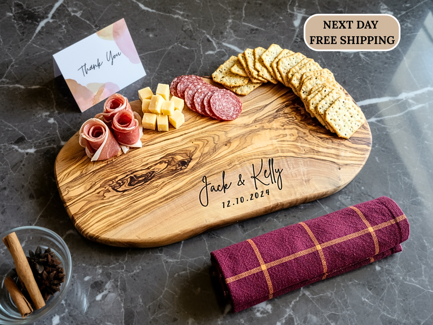 Wooden cutting board with personalized engraving, meats, cheese, and crackers on a dark surface.